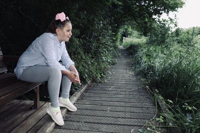 Side view of girl sitting on footpath amidst plants