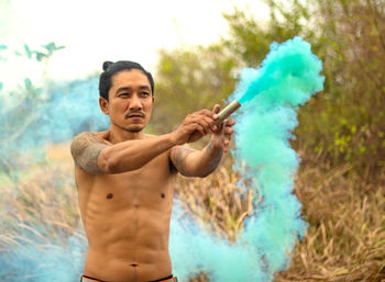 Shirtless man with distress flare standing in forest