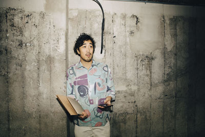 Portrait of young man using phone while standing against wall