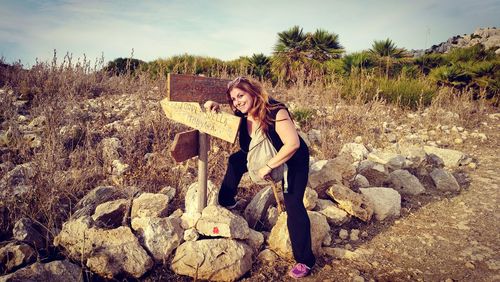 Portrait of smiling woman standing by signs on rocks