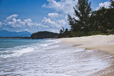 Waves of the azure andaman sea under the blue sky reaching the shores of cenang beach in langkawi