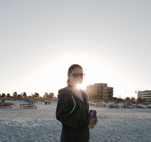 Woman standing at beach against sky during sunset