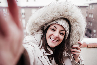 Happy woman on terrace at home enjoying snow while taking selfie with mobile phone