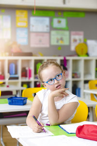 Thoughtful girl writing in paper at kindergarten