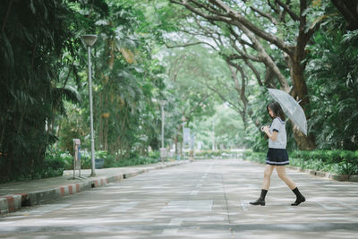 Side view of young woman with umbrella walking on road