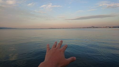 Hand on sea against sky during sunset