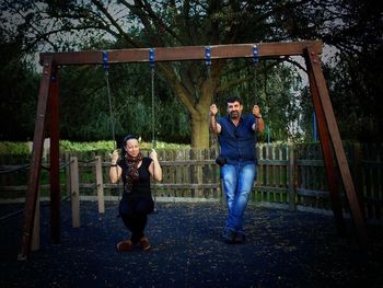 Portrait of mature friends sitting on swing at park