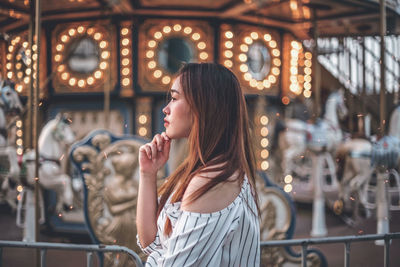 Woman looking away while standing by carousel