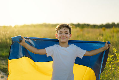 Ukrainian child boy in white t shirt with yellow and blue flag of ukraine in field.