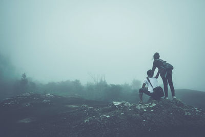 Couple on mountain against sky during foggy weather