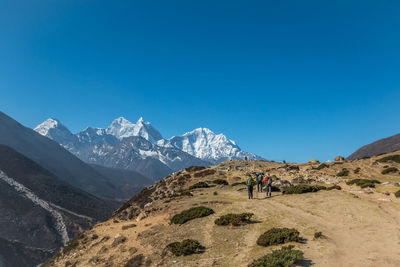 People on snowcapped mountain against blue sky