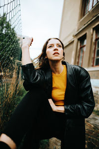 Thoughtful young woman standing by fence