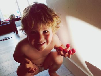 Portrait of smiling shirtless boy holding raspberries at home