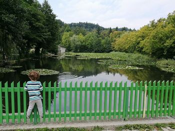 Rear view of boy standing on fence against lake