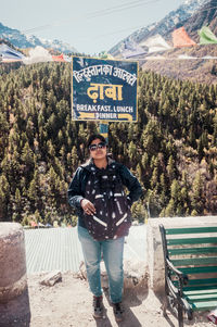 Full length portrait of woman standing against text ad trees