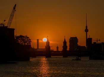 Silhouette of buildings by river during sunset