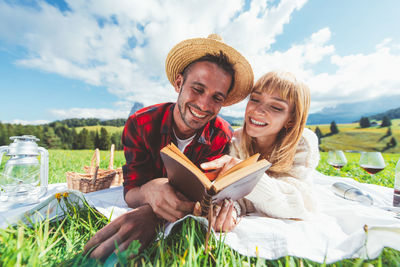 Happy young couple sitting against sky