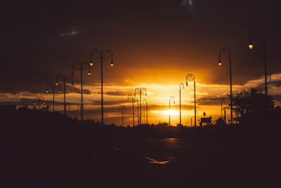 Silhouette city street against sky during sunset