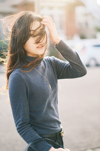 Young asian girl looking away while standing outdoors in sunlight. 