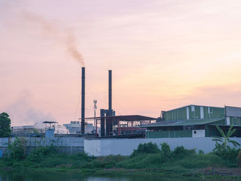 Industry factory building with smoke and steam from smokestack near river against twilight sky