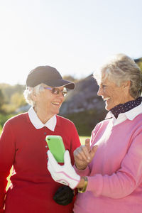 Smiling senior female golfers using mobile phone on golf course