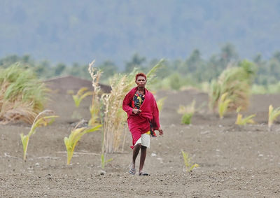 Full length portrait of smiling young woman standing against trees