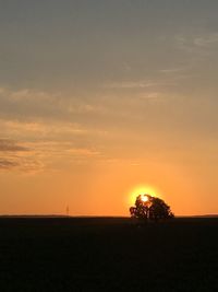 Silhouette trees on field against orange sky