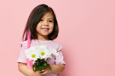 Portrait of young woman holding flower against pink background