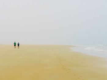 Rear view of men jogging at shore of beach against sky