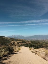 Dirt road amidst landscape against sky