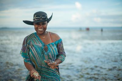 Portrait of smiling woman showing seashells while standing on beach