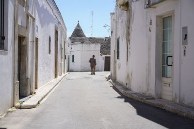 Rear view of man walking on road amidst old houses in town