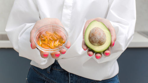 The woman holds avocado and yellow capsules with vitamin d and omega-3. health and diet.