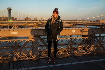 Portrait of young woman standing on railing against bridge