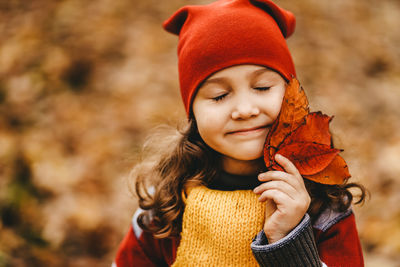 Portrait of a little girl a child in a warm hat walking holding an autumn foliage in the fall forest