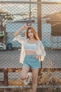 Portrait of smiling young woman standing by chainlink fence