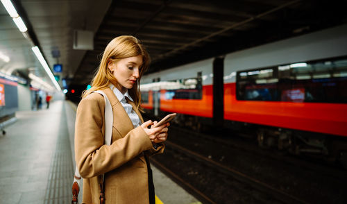 Young long-haired woman messaging phone while standing on the subway