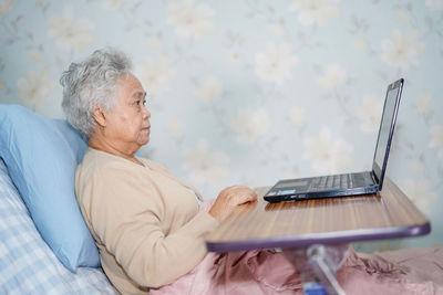 Side view of senior woman using laptop while relaxing on bed