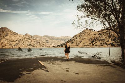 Rear view of woman standing on shore against sky