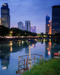 Illuminated buildings by river against sky in city