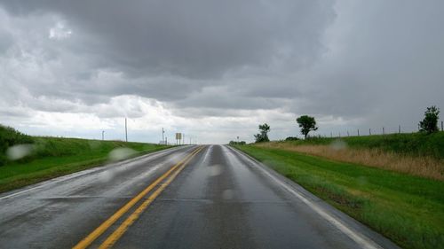 Road amidst grassy field against cloudy sky