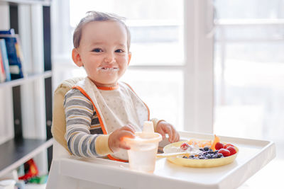 Caucasian baby eating ripe berries and fruits with yogurt. supplementary healthy food for toddler