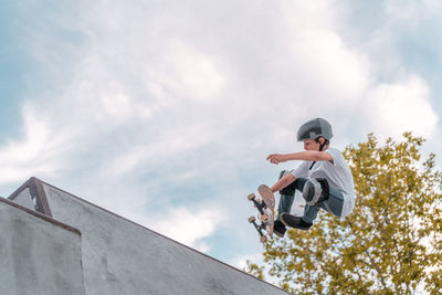 Teenage boy jumping with skateboard and showing stunt on ramp in skate park