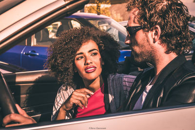 Portrait of happy young woman sitting on car