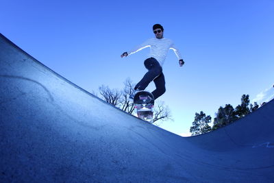 Low angle view of man jumping against blue sky