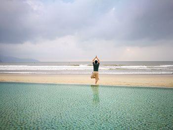 Rear view of man exercising amidst swimming pool and sea at beach