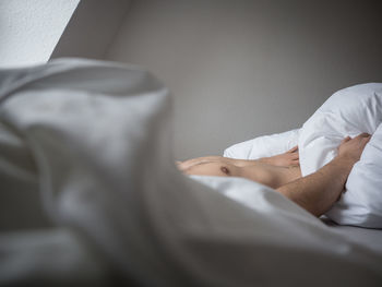 Midsection of shirtless man sleeping on bed at home