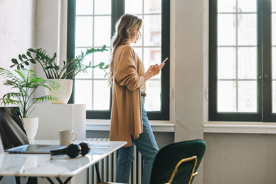 Young woman with long hair in cardigan with mobile in office, woman send message by smartphone