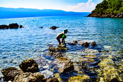 People on rocks by sea against sky