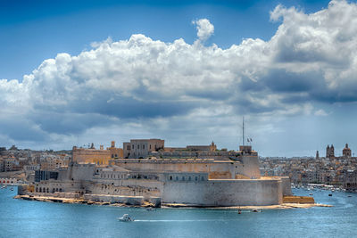 Buildings by river against cloudy sky